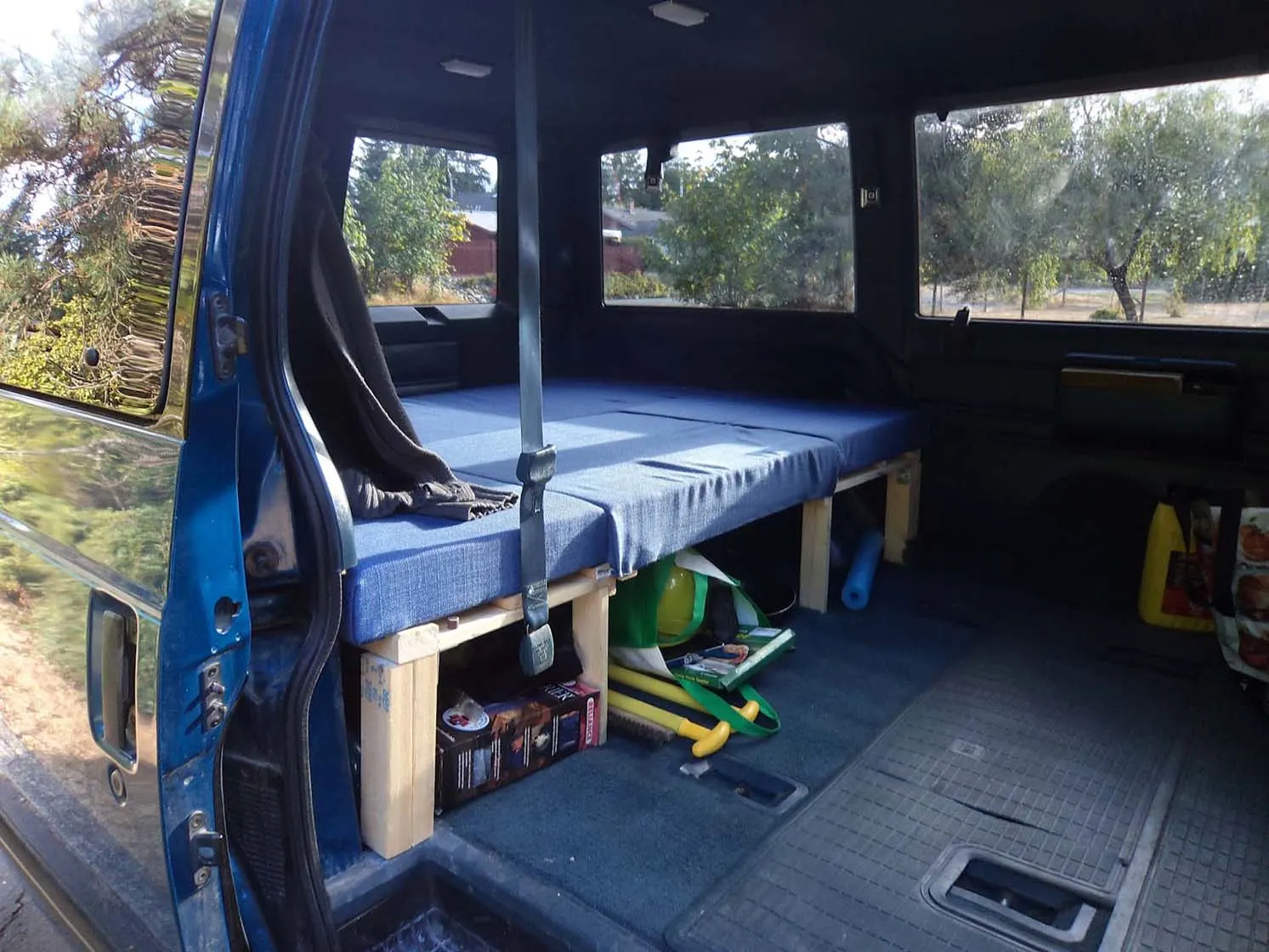 Looking inside a blue Chevrolet Astro Van. It has a bed frame with blue cushion in it.