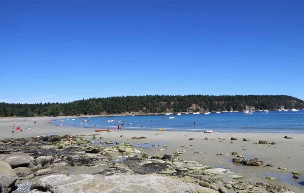 Looking across rocks to sandy Tribune bay, one of the best BC beaches. There are many people in the beach and in the calm ocean