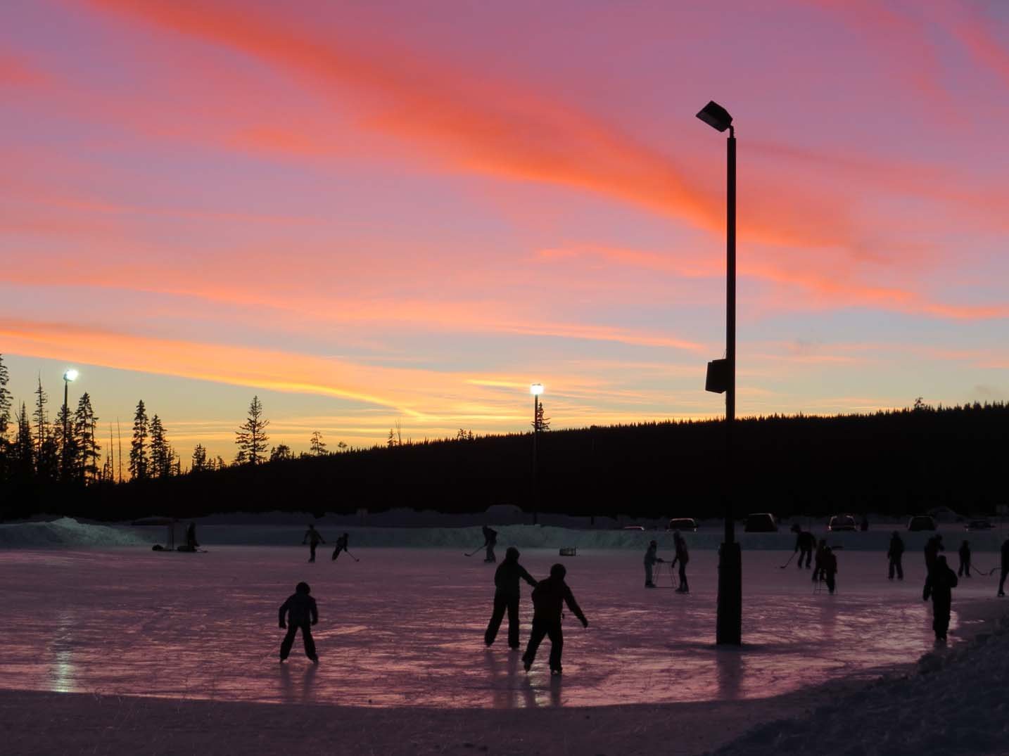 Ski rink at sunset with silhouettes of skaters