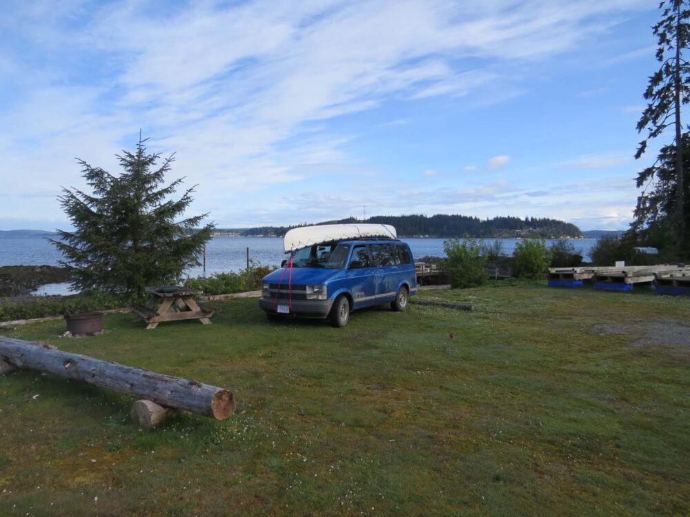 Blue van is parked in a campsite with ocean views at Alder Bay campground