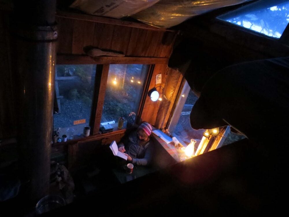 Gemma reading by wood stove in cabin