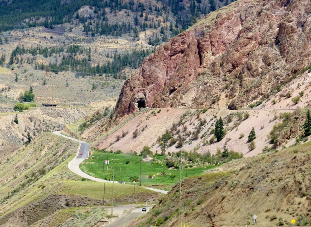 Dry desert landscape with highway on left and railway line on right. There is a tunnel blasted through the rock