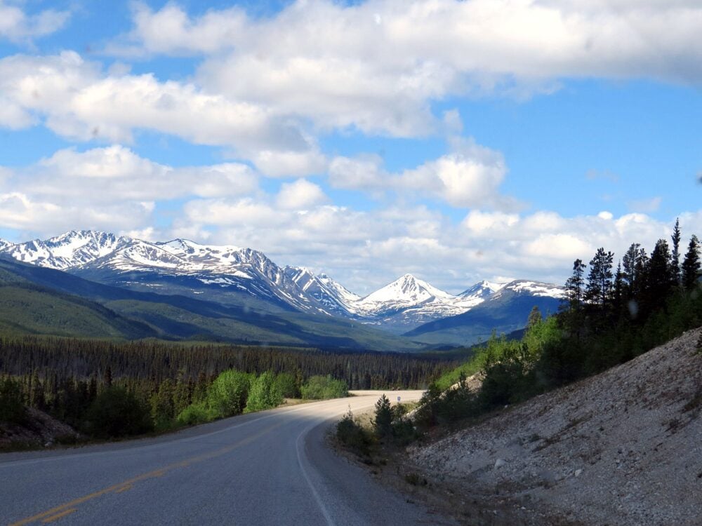 Driving a road in Yukon, with mountains in the background and trees in the foreground