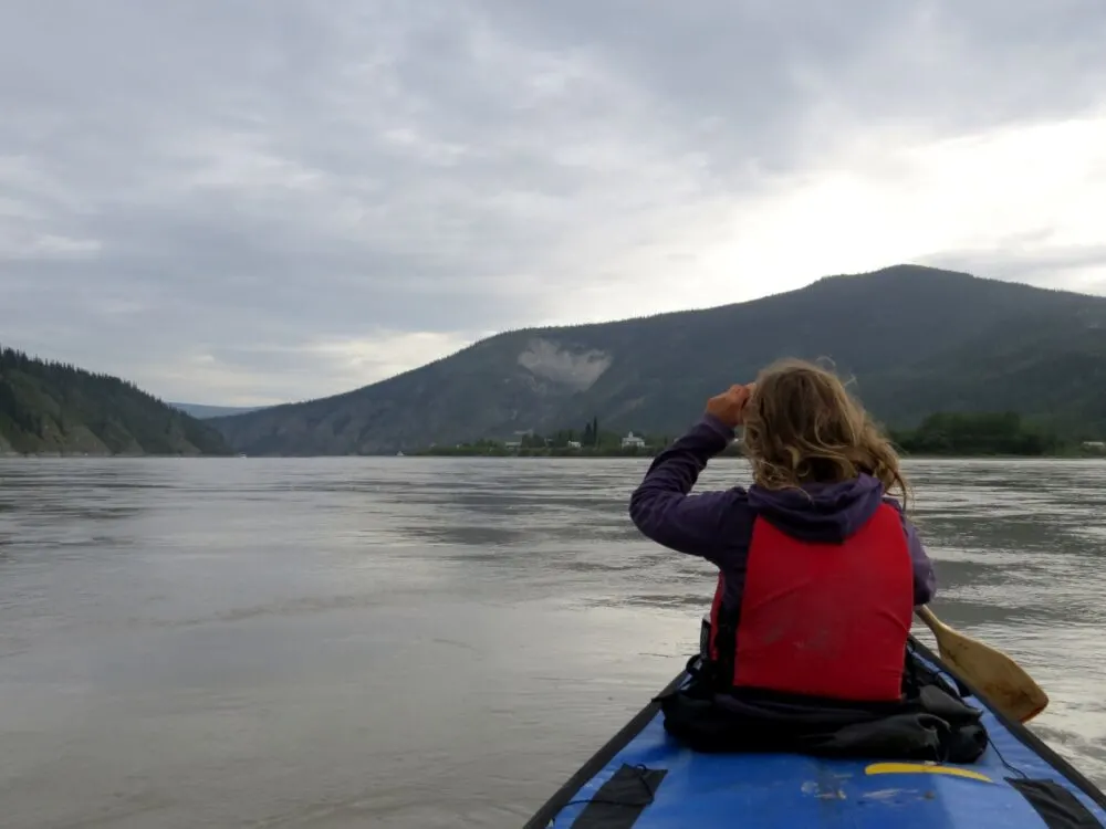 Gemma paddling at the front of the canoe, looking out to Dawson City, Yukon, in the distance