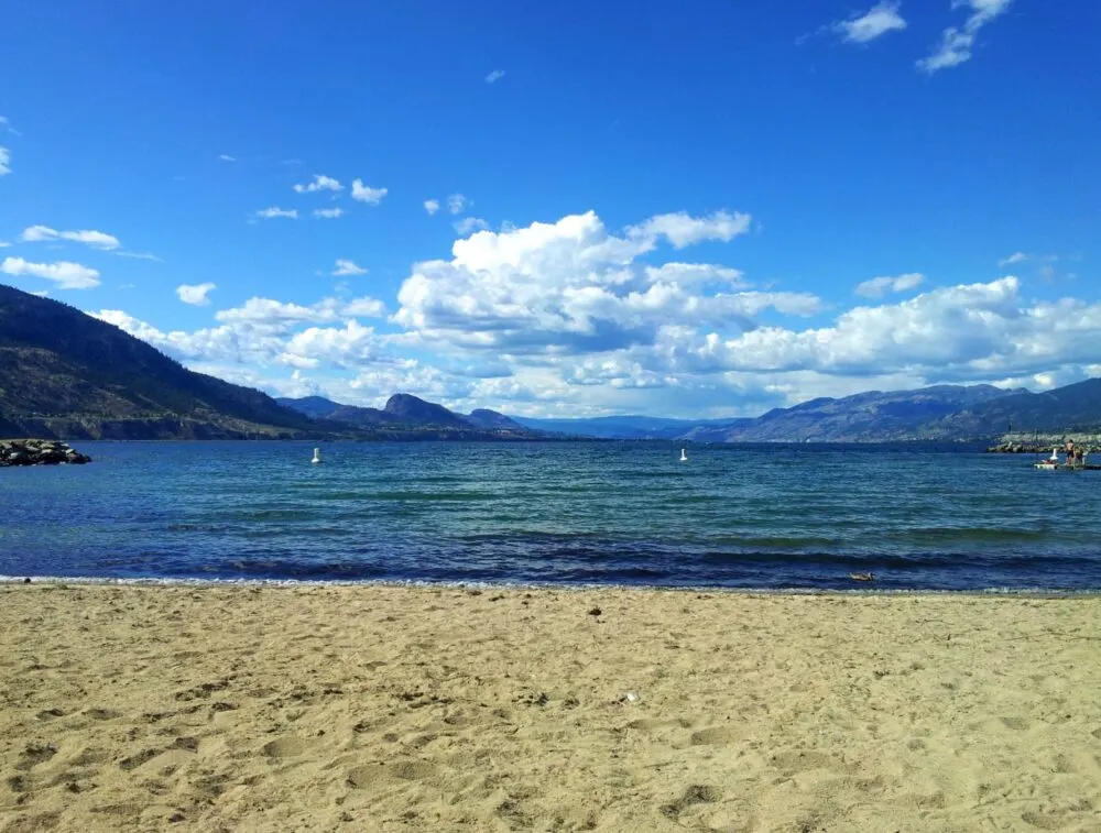 Sandy Okanagan lake beach with calm water and valley hills behind