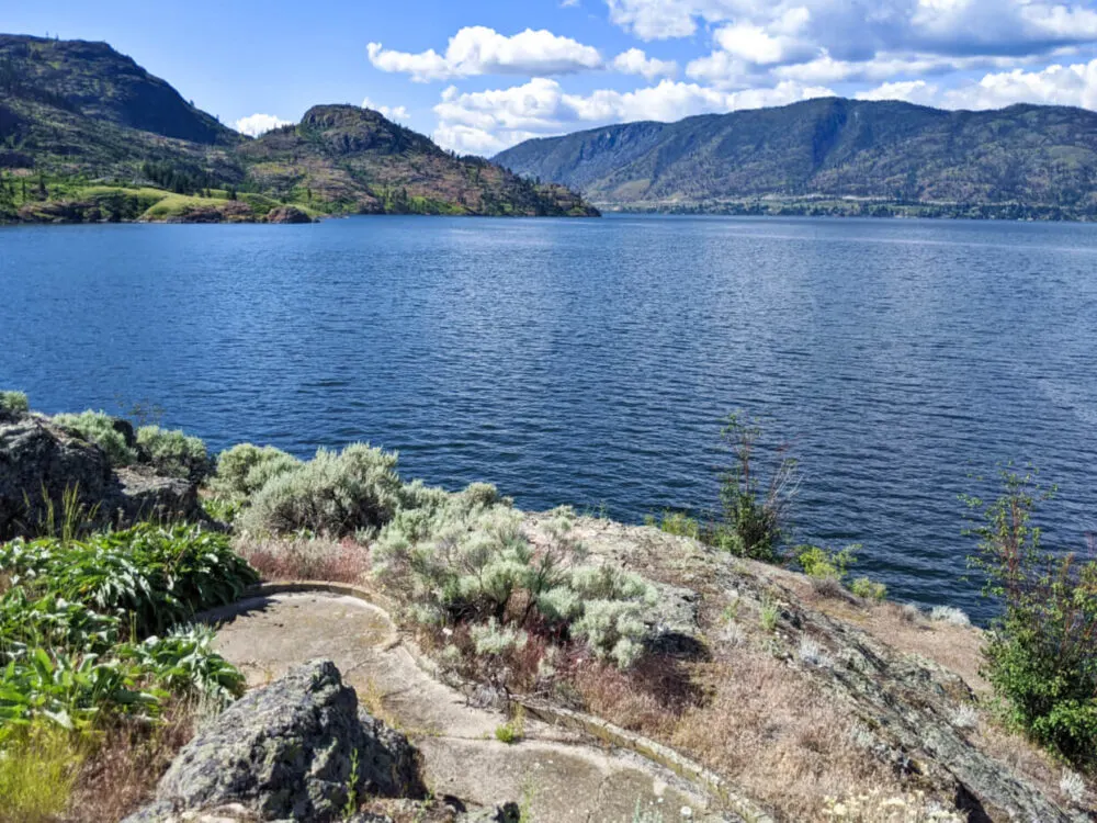 Concrete miniature golf hole surrounded by shrubby landscape, backdropped by Okanagan Lake and rugged landscape of Okanagan Mountain Park