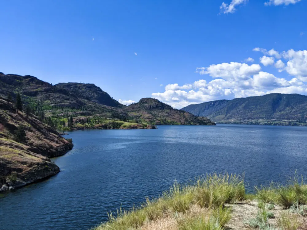 Looking across from elevated viewpoint on Rattlesnake Island towards Okanagan Lake and Okanagan Mountain Park, which has a curving shoreline with rugged mountainous terrain above