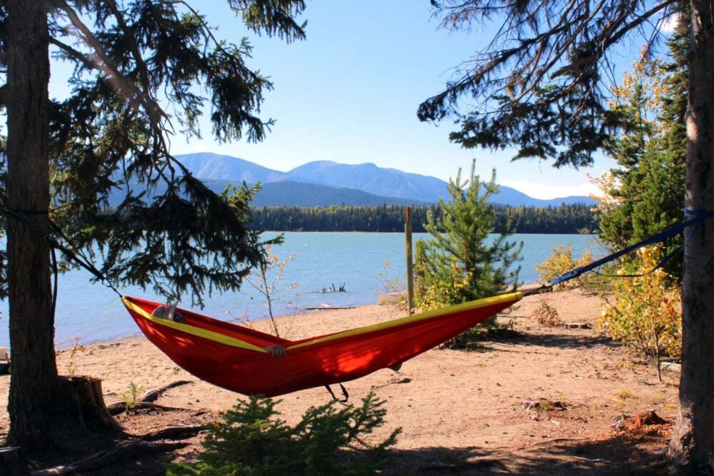 Orange, red and yellow hammock hanging between two trees next to calm lake