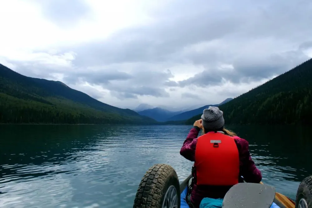 Back view of Gemma paddling on Isaac Lake, with mountains and rain in the distance