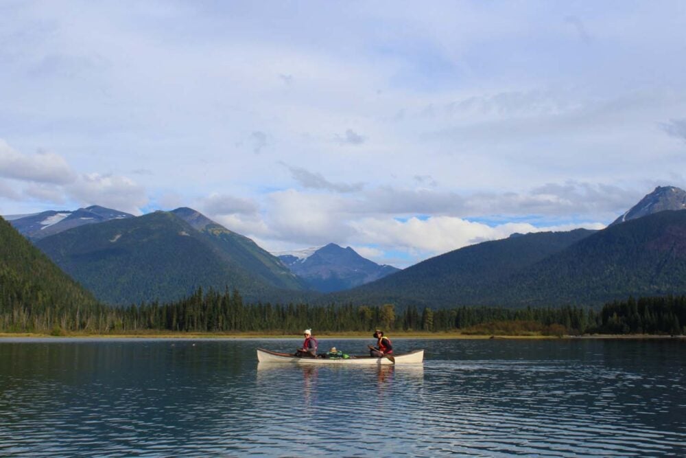 White canoe with two paddlers on calm lake with mountain background