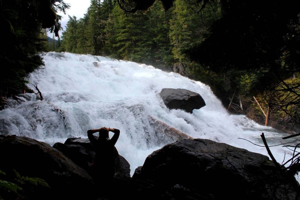 Gemma standing with arms on head in front of fast flowing Isaac River Falls