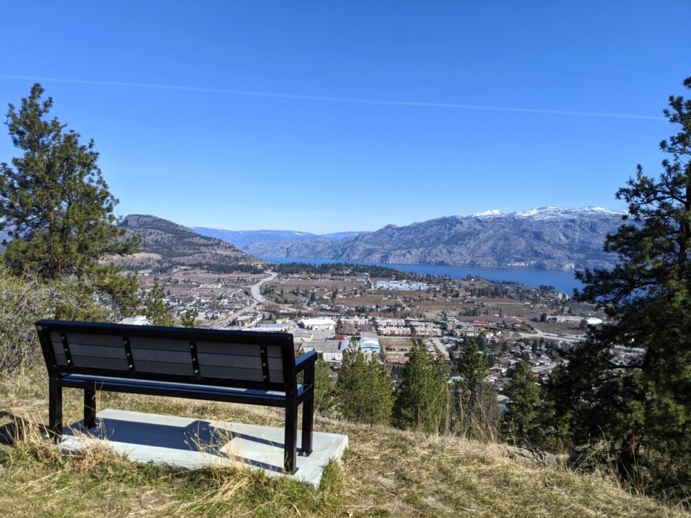 Bench looking out over elevated view of Summerland township with Okanagan Lake and snow capped mountains in background on Giant's Head Mountain Roadway trail