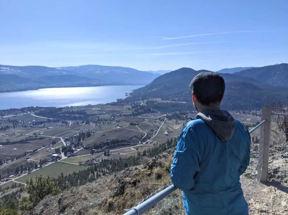 JR standing behind fence, looking out over Okanagan Lake, Highway 97 from the top of Giant's Head Mountain