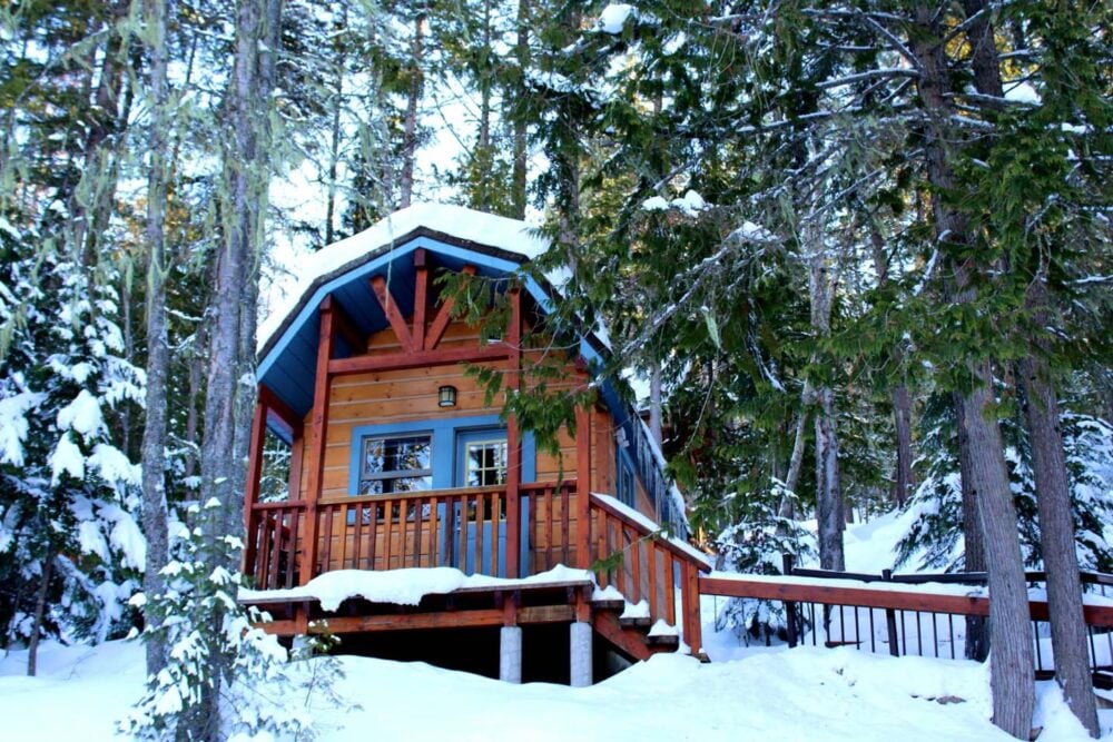 Looking up to a cute cabin surrounded by forest and snow