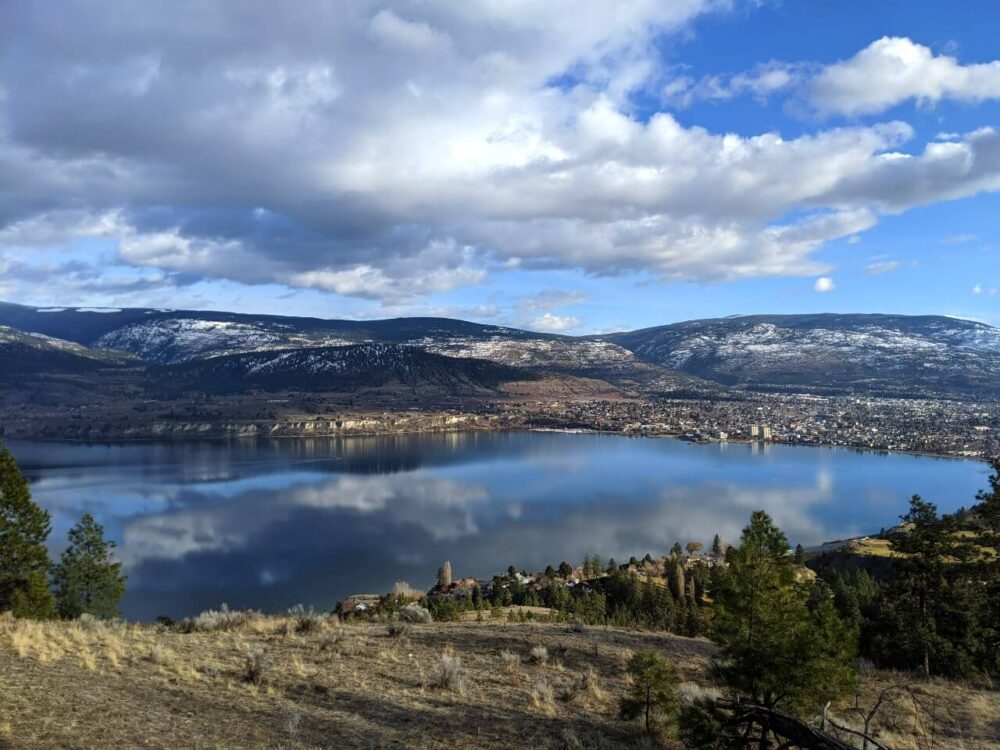 Elevated view looking down on Okanagan Lake and the city of Penticton on right. There is snow in the higher hills behind
