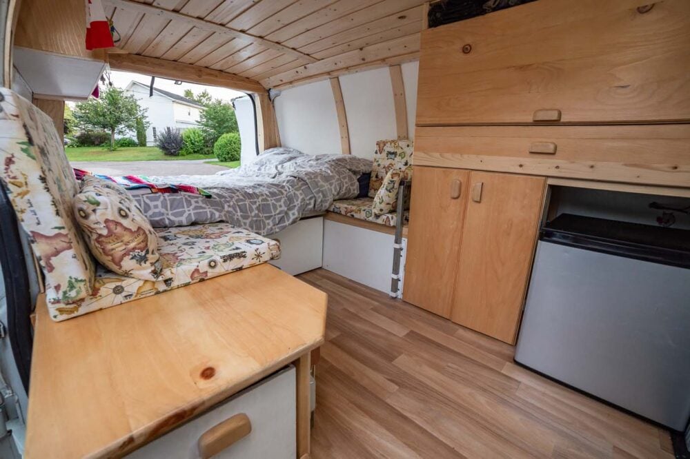 Finished van conversion with white panel walls, wood ceiling, lino, kitchen counter, cupboards, fridge