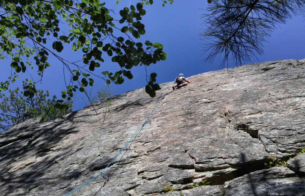 Looking up at a climber on Go Anywhere wall at Skaha Bluffs on a sunny day