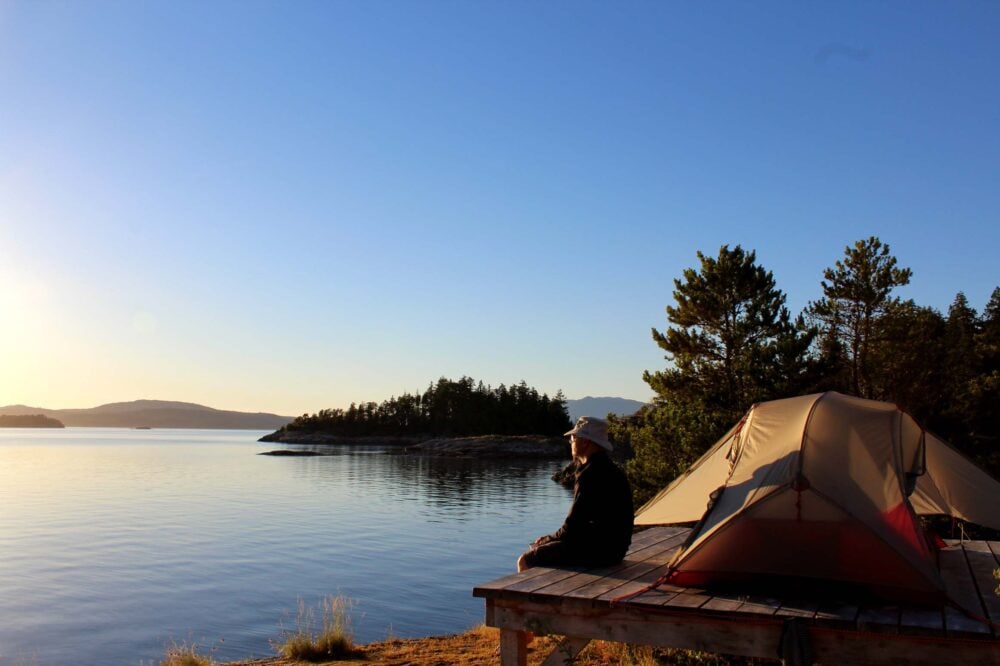 JR sat next to tent platform on Sunshine Coast, British Columbia, with ocean visible to the left