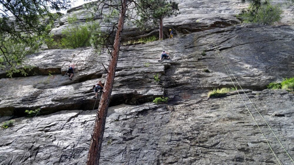 Looking up at Red Tail climbing wall at Skaha Bluffs, British Columbia, with rock wall, ropes and climbers