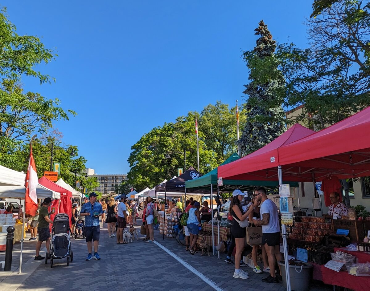 Looking down stalls at Penticton Farmers Market on a sunny summer day