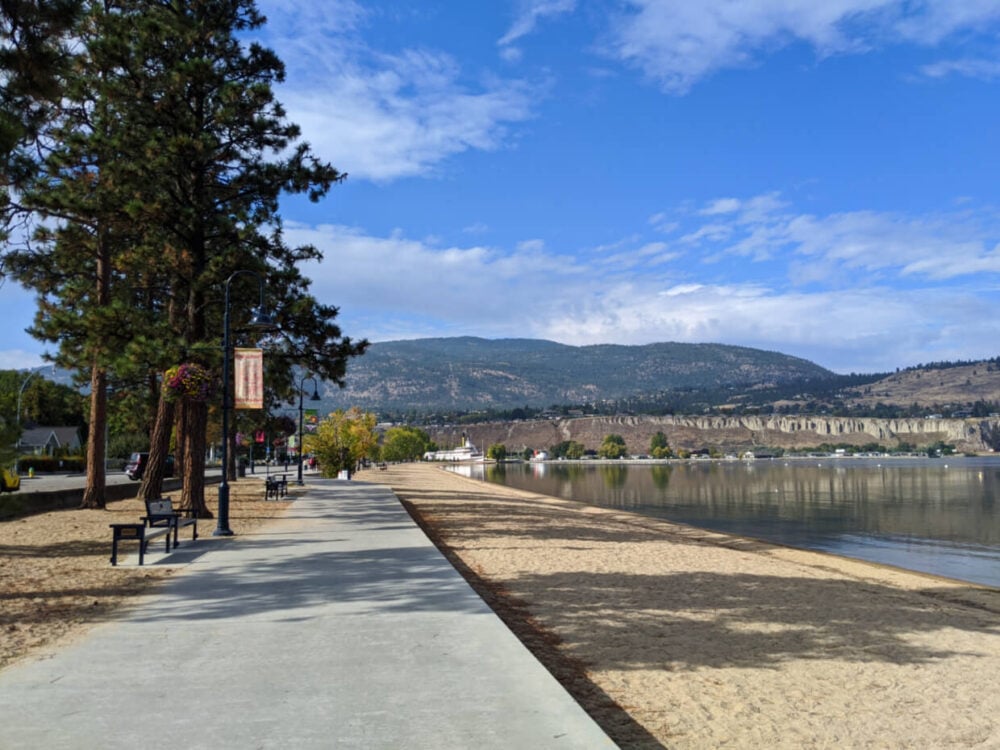 Concrete walking path next to sandy beach and calm lake in Penticton