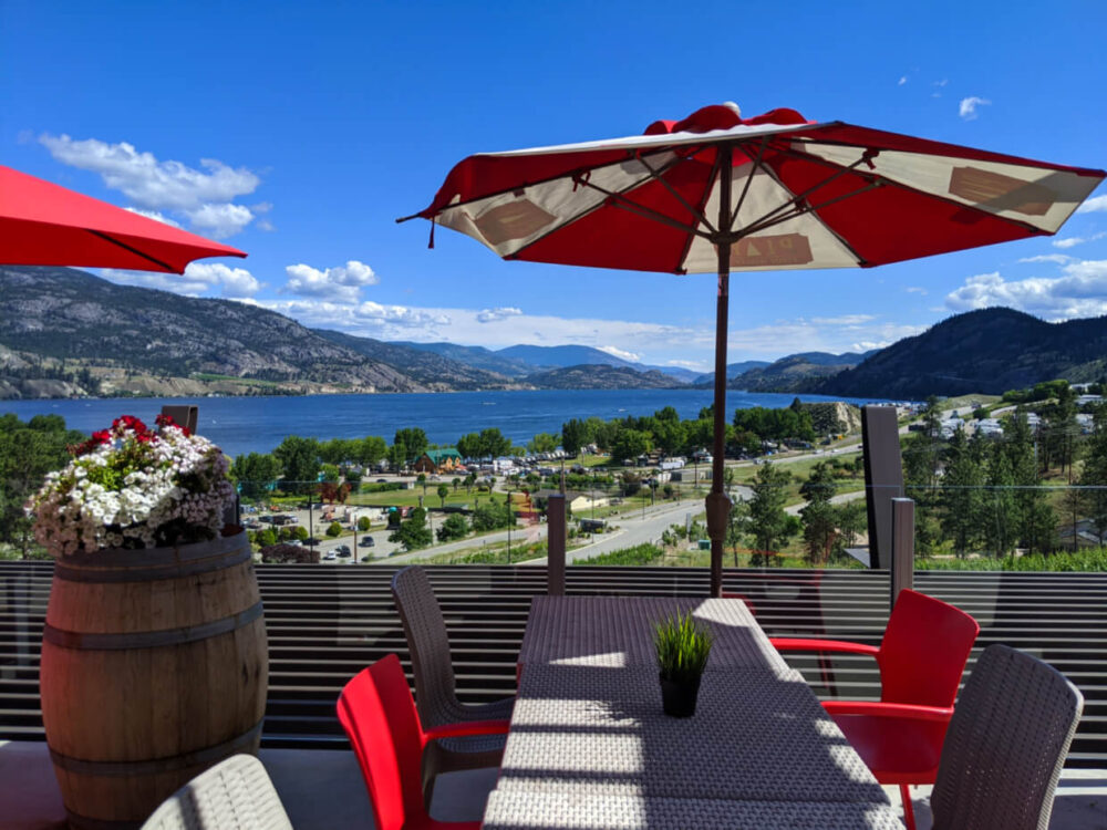 Chairs, table and umbrella on Play Winery patio in front of Skaha Lake 