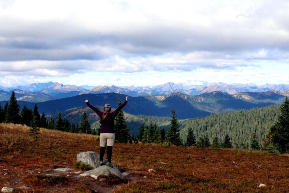 Back view of Gemma standing on rock, looking out to incredible mountain views on the Heather Trail