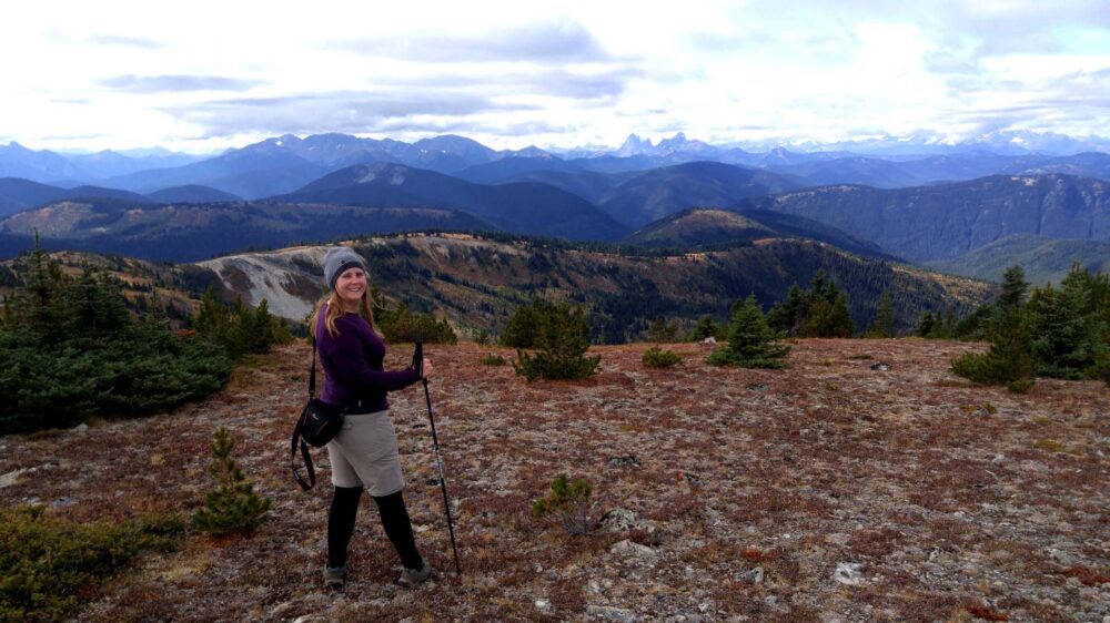 Back view of Gemma standing with hiking pole in front of mountainous landscape