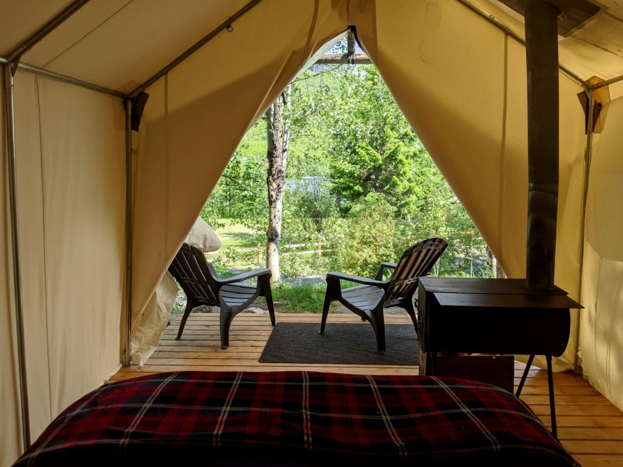 Looking from the bed outside in one of Chute Lake Lodge's Glamping tents, with wood stove and chairs on deck