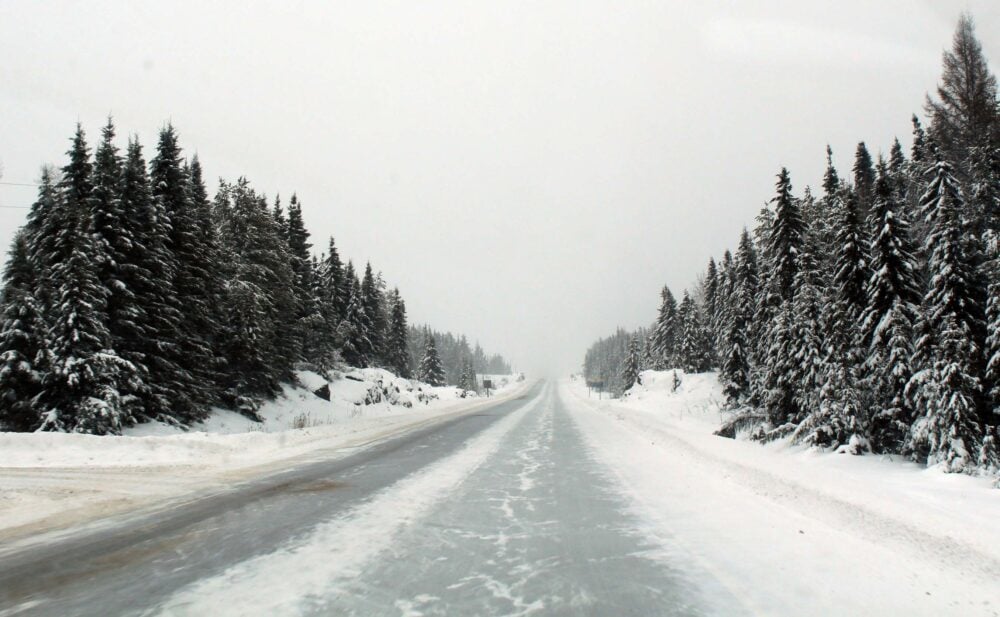 Snowy road conditions in Ontario, vehicle windshield view of snowy road with snowy surrounding forest