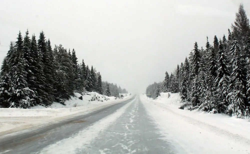 Snowy road conditions in Ontario, vehicle windshield view of snowy road with snowy surrounding forest