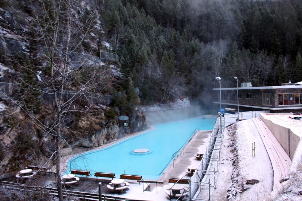 View of Radium Hot Springs swimming pool from highway in winter, with large pool next to steep forested hill