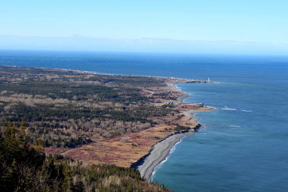 High view of Gaspe Peninsula beach and rocky coastline with lighthouse at end