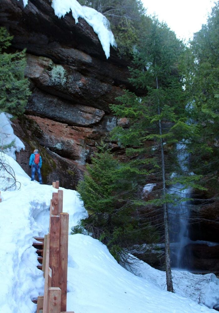 Looking up to JR on snowy trail in the Grotto in Perce, with huge eroded cliffs above