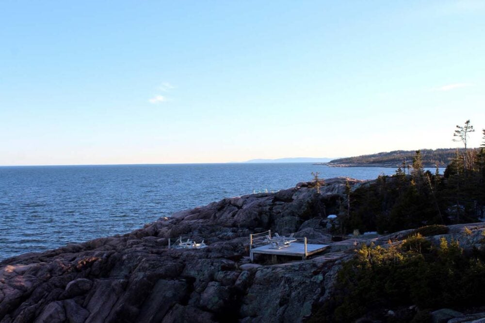 Looking across rocky shoreline at Mer et Monde at sunset, where there are a number of wooden tent pads with panoramic ocean views