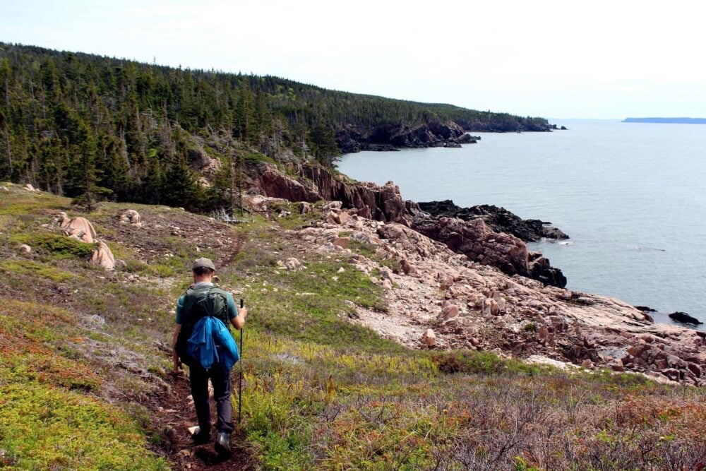 JR hiking along dirt path with hiking pole with coastal views beyond