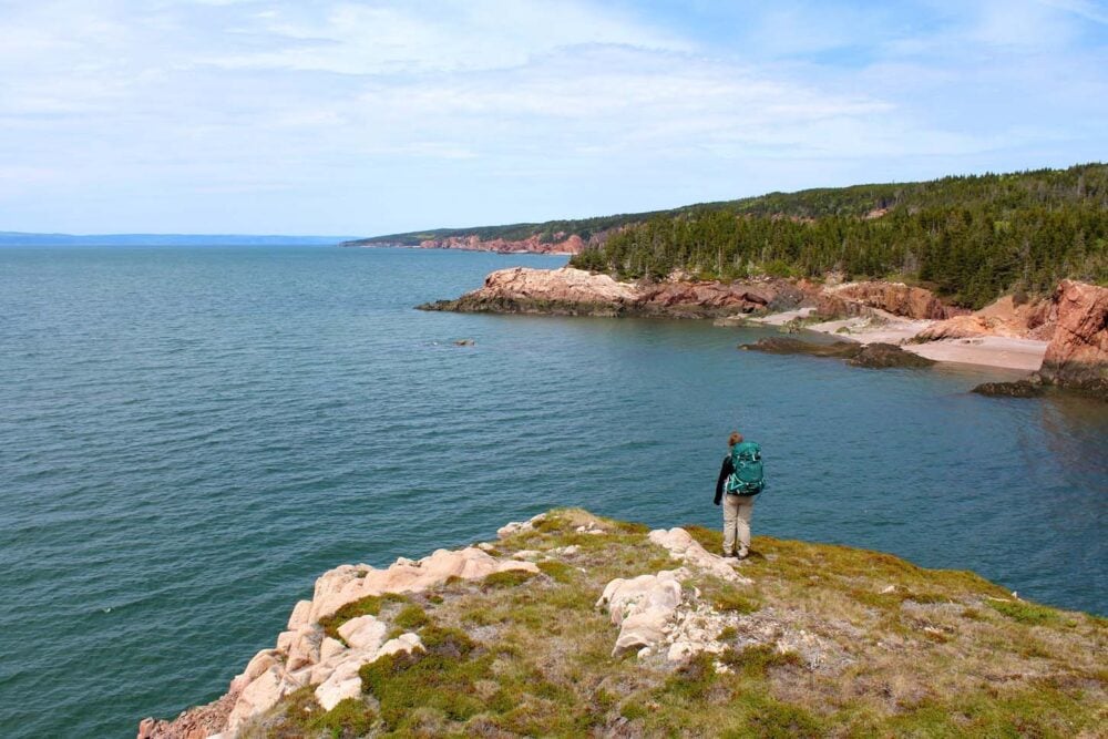 Gemma standing on rocky headland looking back at Nova Scotia coastline on the Cape Chignecto Trail