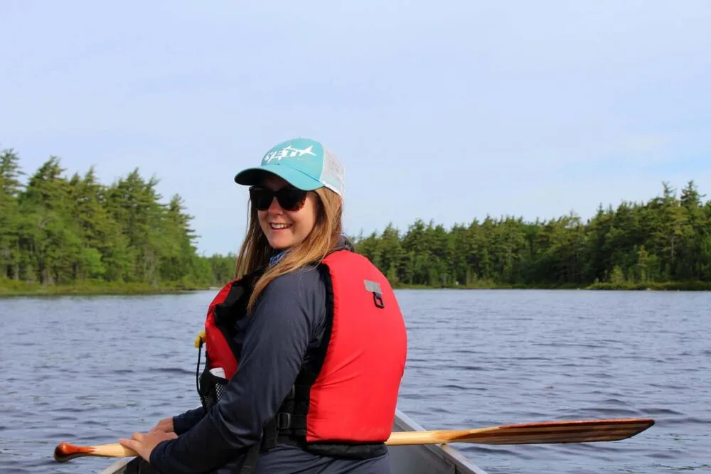 Back view of Gemma set in front of canoe in Kejimkujik national park, on calm lake. Gemma is turning around and smiling at camera