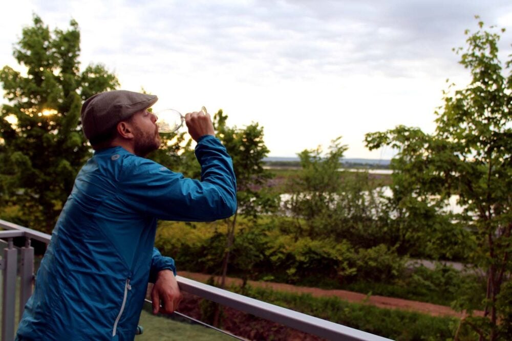 JR is leaning on the balcony at Micro Boutique Living and drinking a glass of wine, with views of the agricultural dykes behind