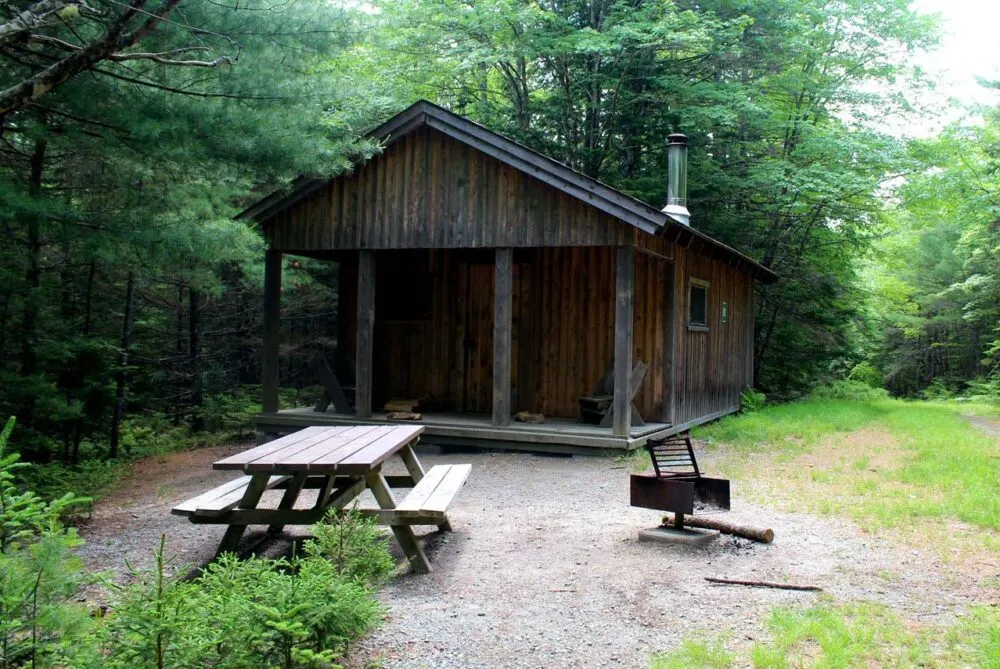 Front view of rustic wooden cabin with picnic table and fire grate in Kejimkujik National Park