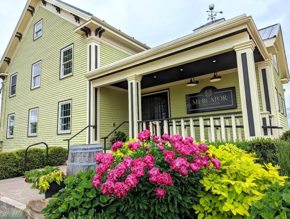 Mercator Vineyards tasting room, a yellow three story farmhouse style building with colourful flowers in front