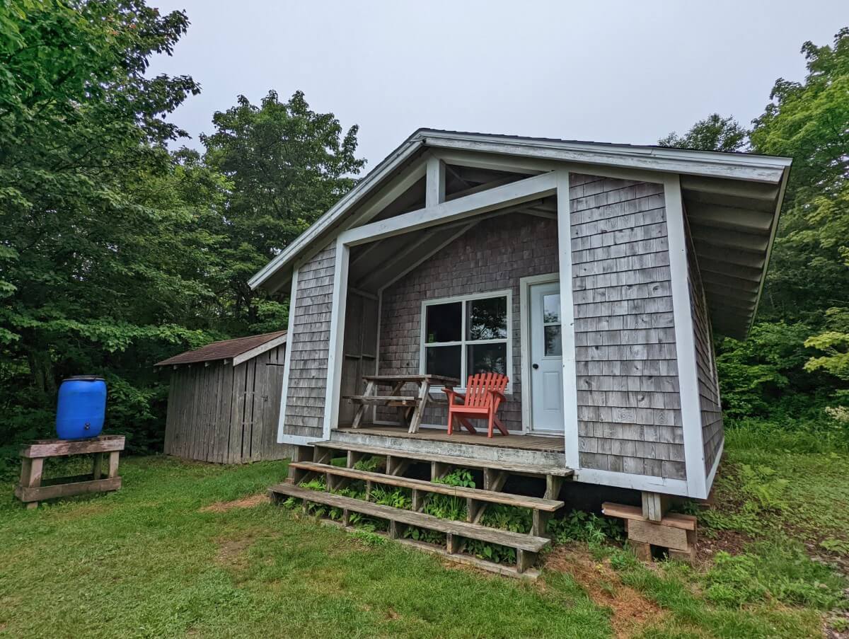 Arch Gulch Cabin view with three steps leading into small wooden cabin, a picnic table and chair on deck in front