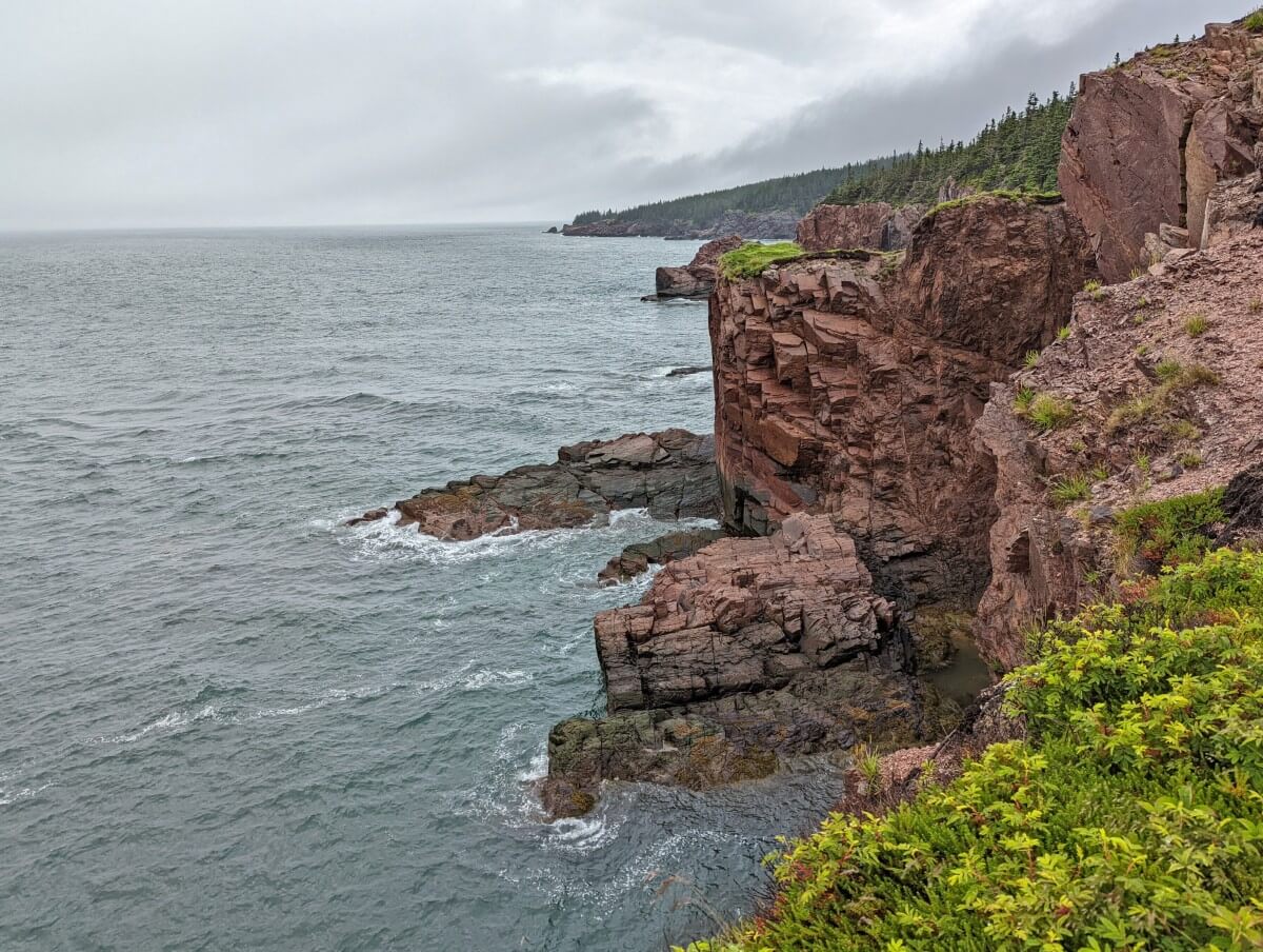 Side view of red tinged rock cliffs on the Cape Chignecto Trail, with ocean below