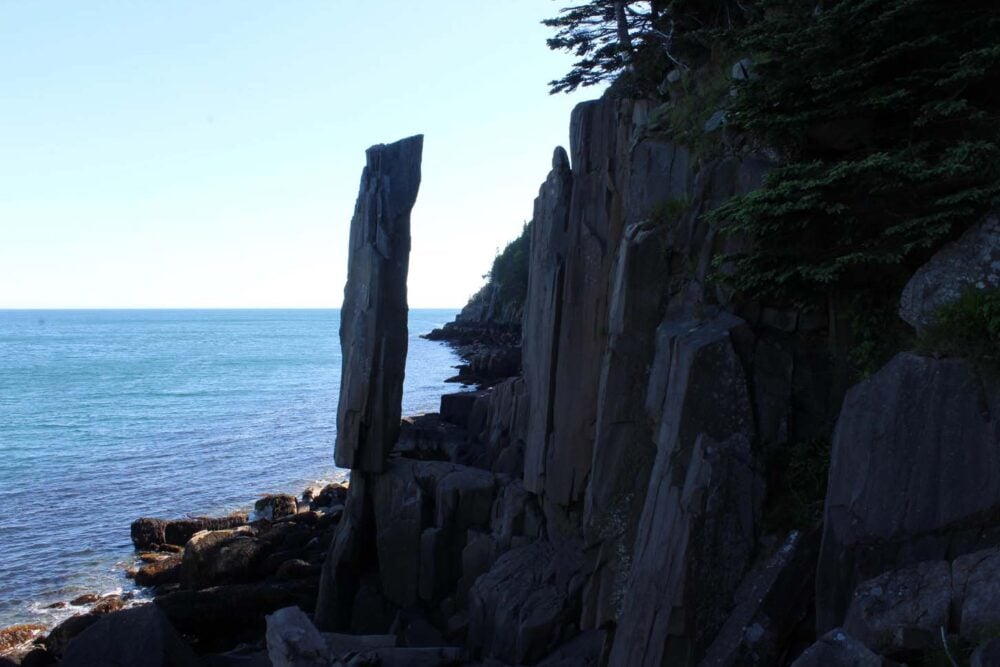 Singular basalt column balancing perilously in the air next to the ocean