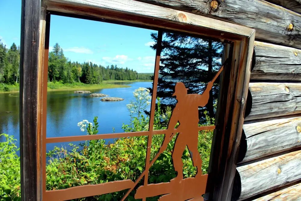 Metal silhouette of farmer set into a cabin window in Lac Temiscoutata Jardin of Memories, with calm lake visible in background