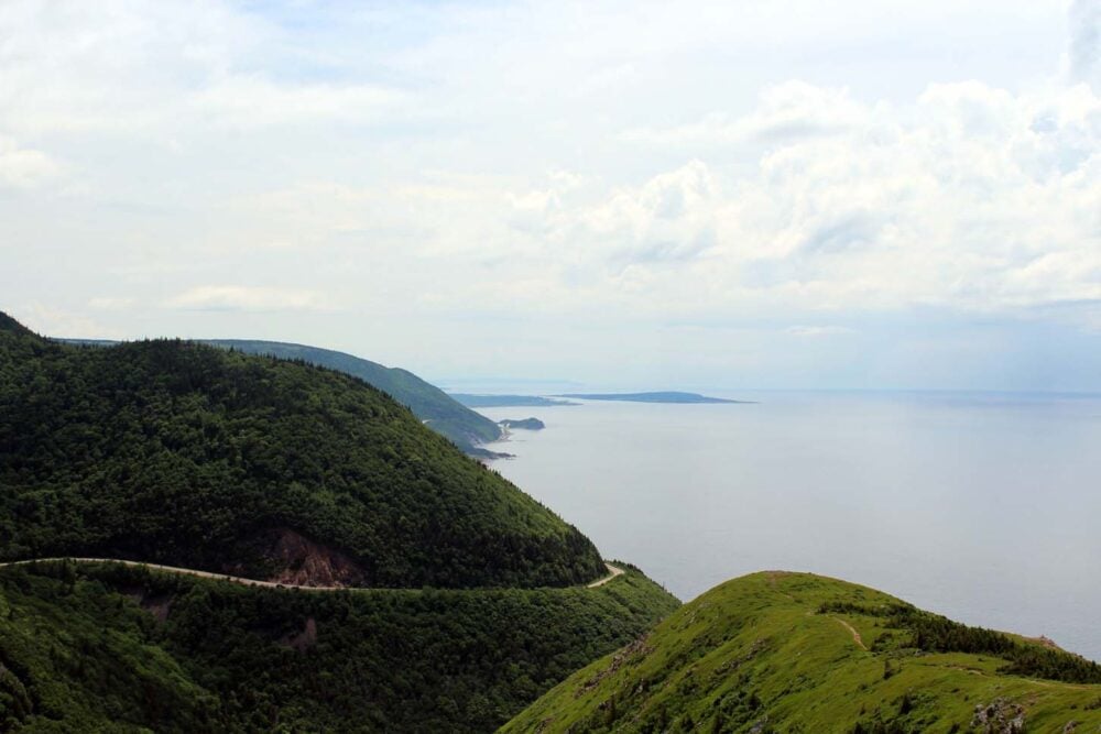 Looking down on a curved road traversing around mountain from the Skyline Trail in Cape Breton Highlands National Park. The scene is backdropped by ocean