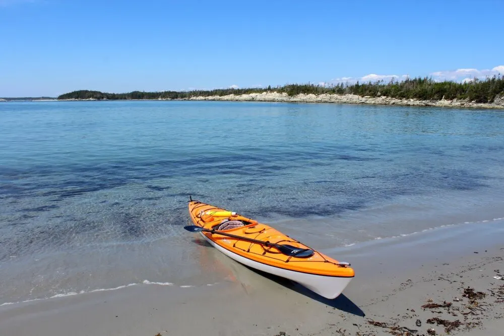 Orange kayak half on sand, half floating on turquoise ocean