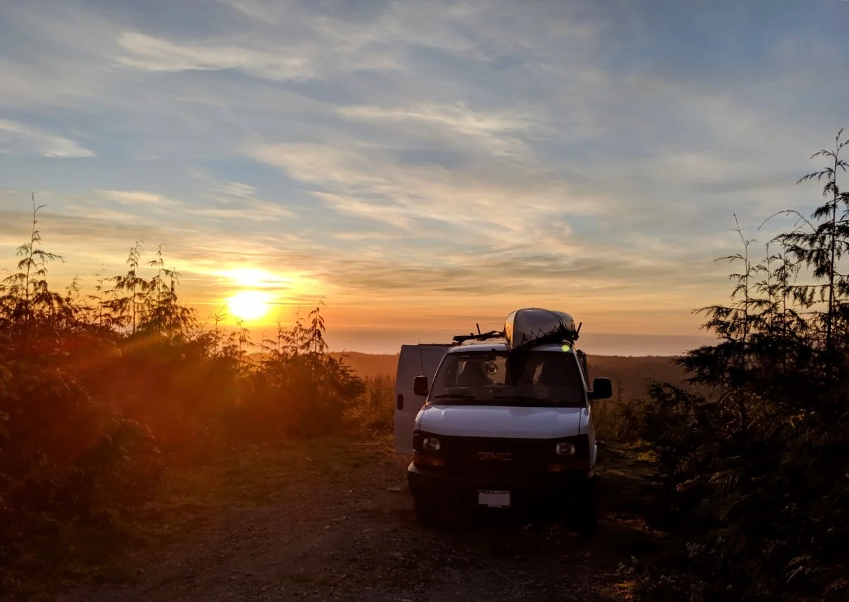 White van parked at viewpoint looking out to a sunset over the ocean