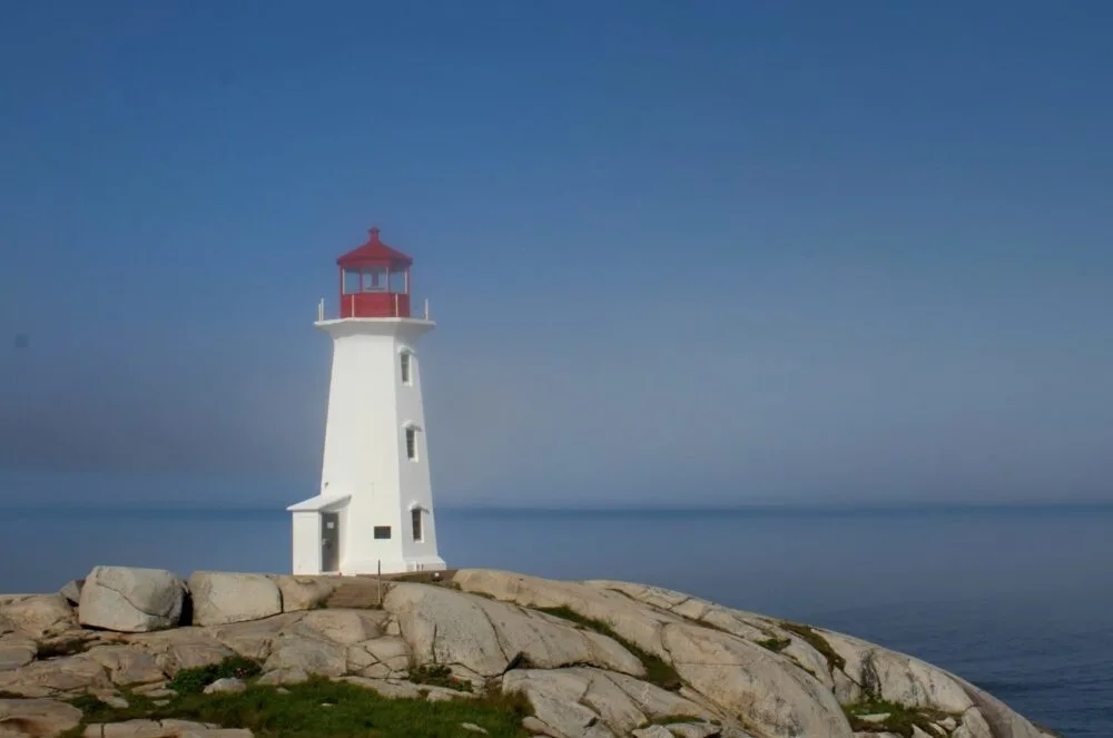 The iconic red and white lighthouse at Peggy's Cove, looking out to the ocean from granite rocks