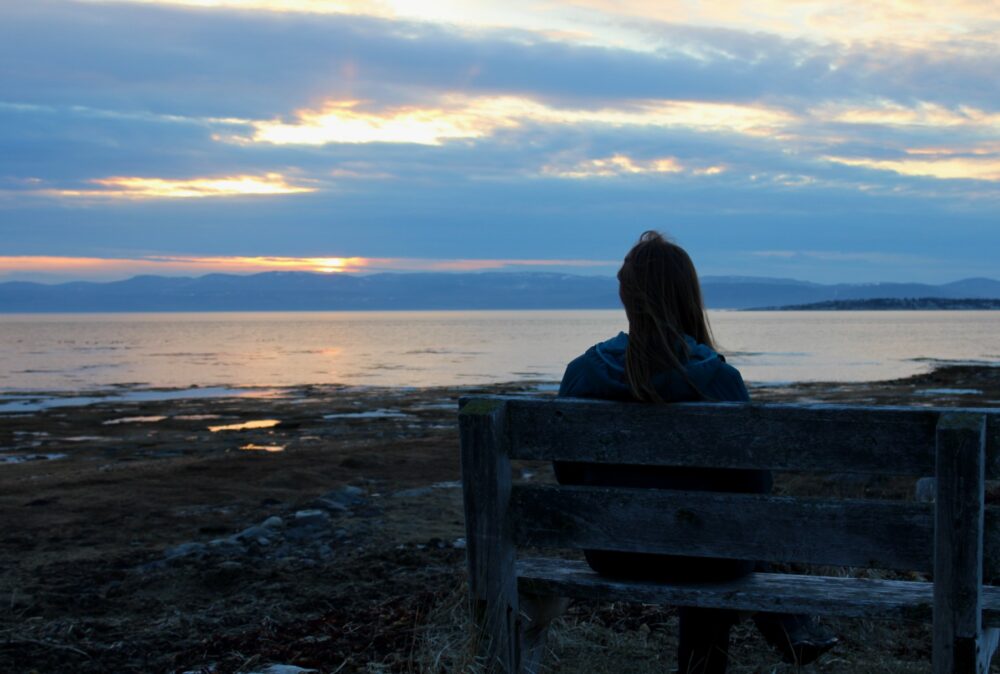 Gemma sat on bench watching sunset over St lawrence river in Quebec